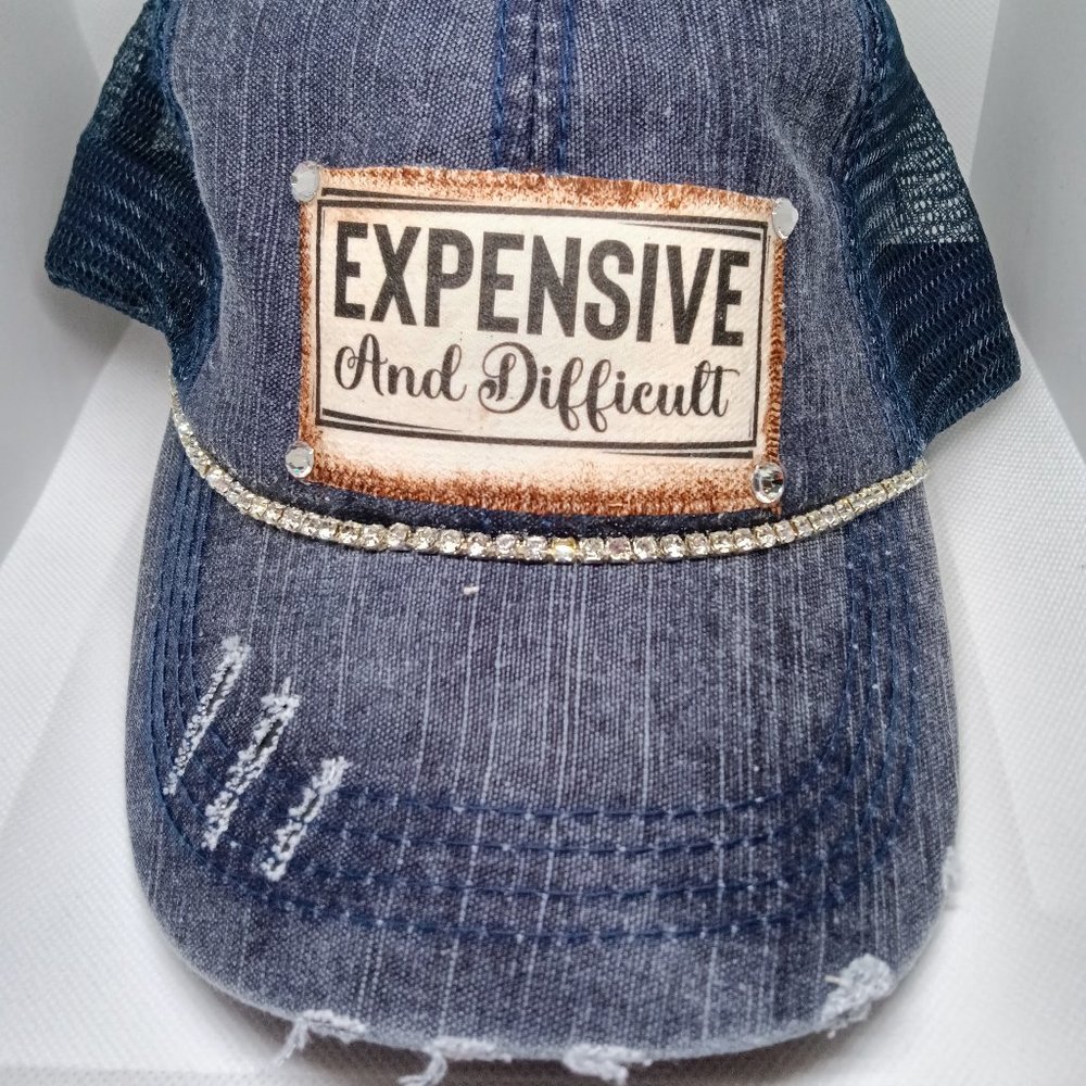 A distressed cap detailed with the saying "EXPENSIVE And Difficult"